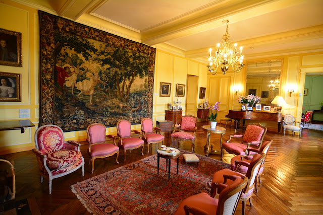 Le salon est organisé autour du piano à queue sur lequel sont posés des portraits de famille ; le décor est du XVIIIème siècle